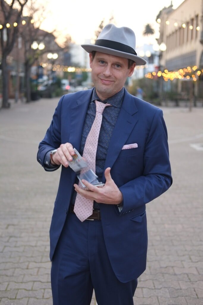 shaun springing cards from hand to hand in blue suit and pink tie.